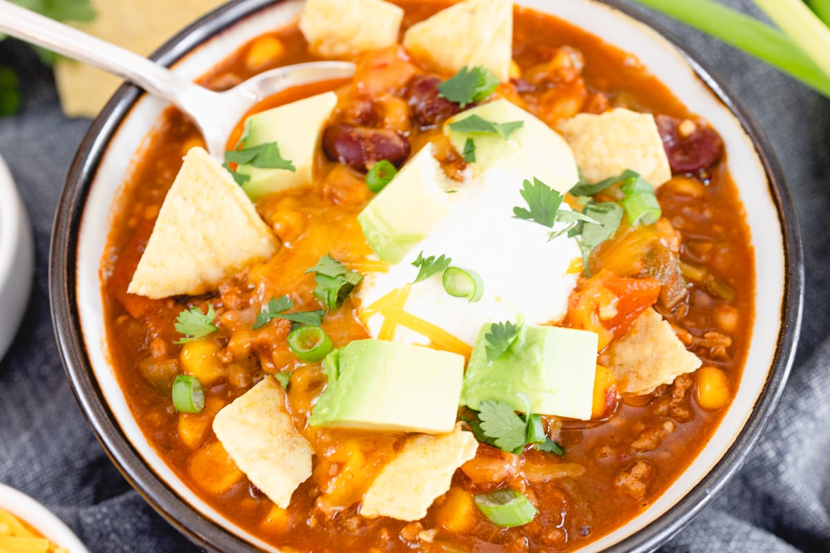 Taco Soup in Bowl with Avocados, Cheese, Sour Cream, Green Onions, Tortilla Chips