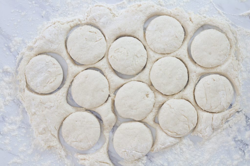 Biscuits cut in dough on floured surface