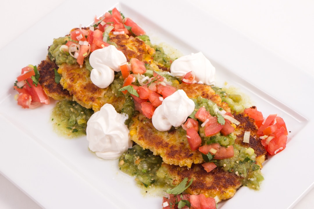 Top view of corn cakes on a serving plate with Mexican toppings on it.