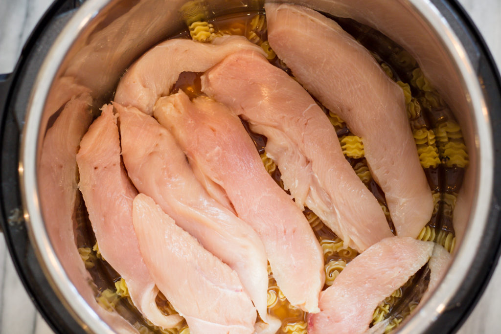 Top view of an instant pot with chicken tenders on top of pasta.