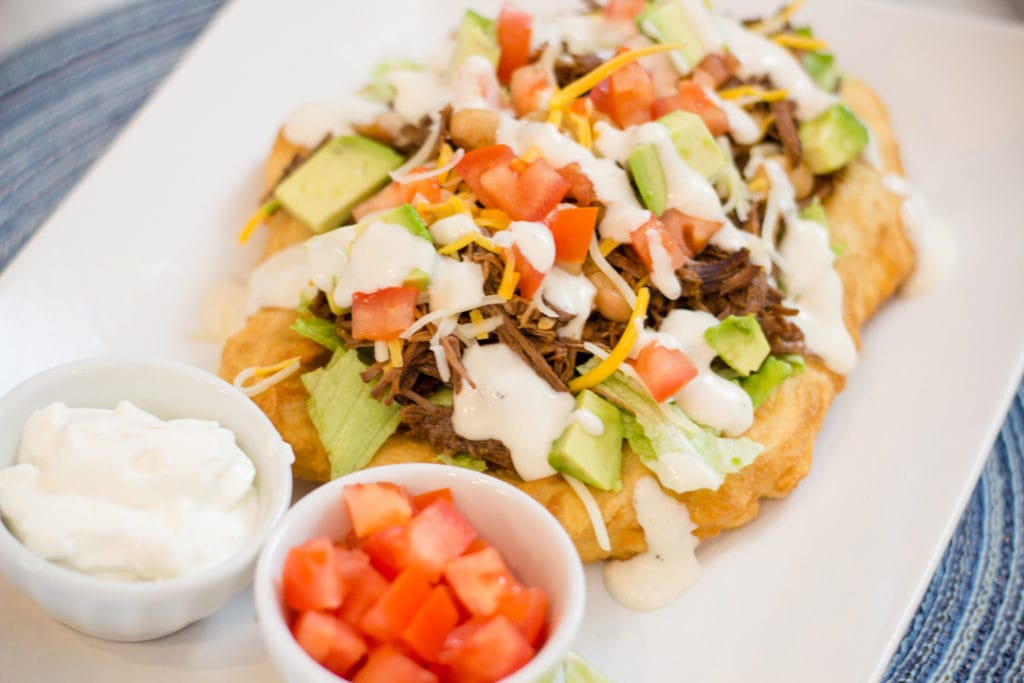 Fry Bread Taco with seasoned meat on white plate with tomatoes and sour cream