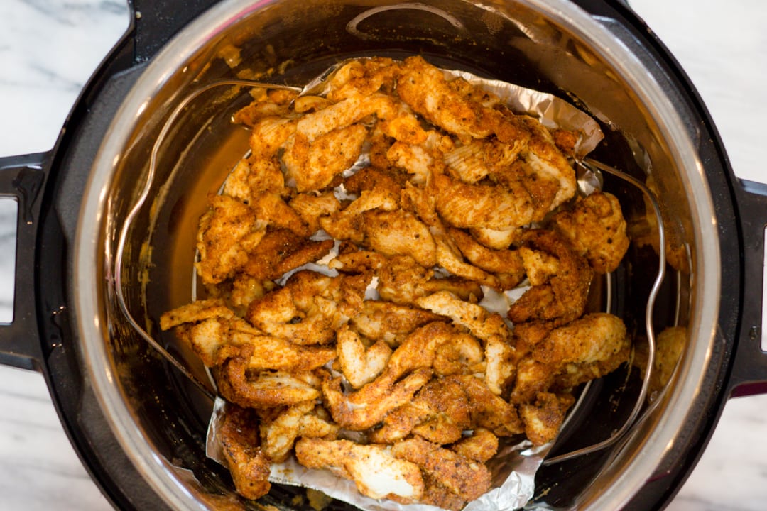 Top view of an instant pot with seasoned chicken in it. 