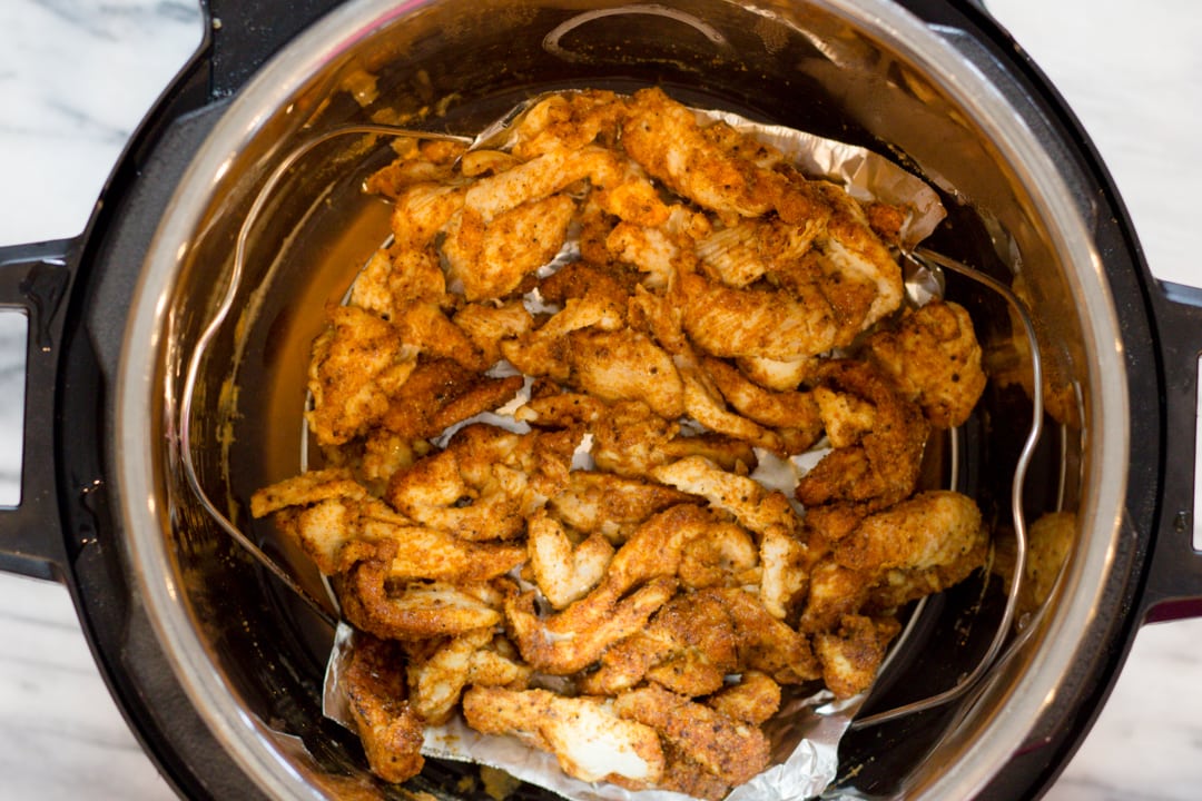 Top view of an instant pot with seasoned chicken in it.