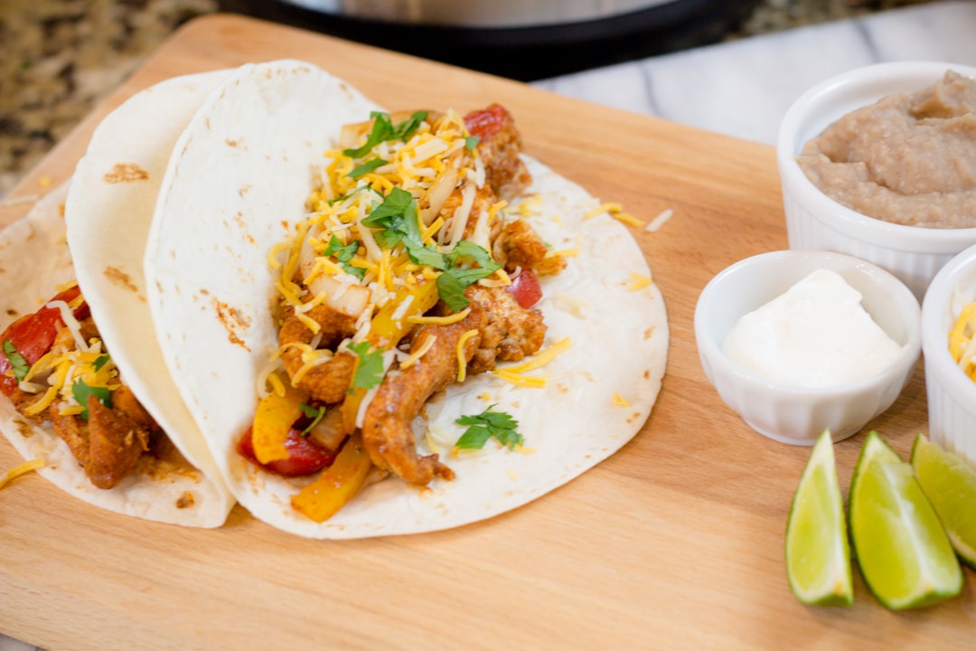 Close up of fajitas on a chopping board next to small bowls with fajita toppings in them.