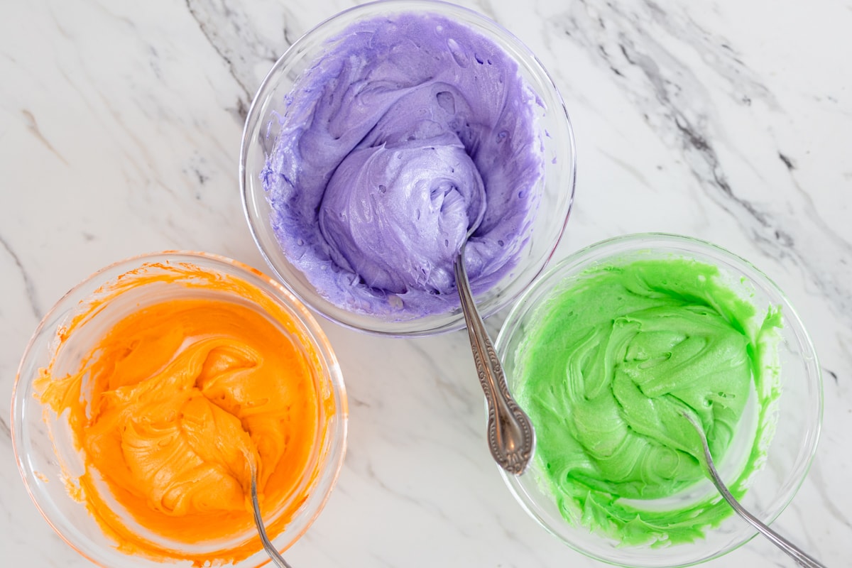 Orange Purple and green bowls of frosting for cupcakes