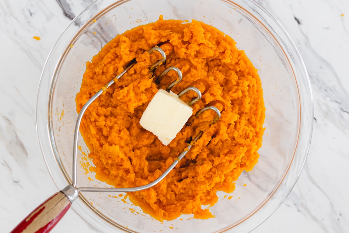 Sweet Potatoes being mashed in bowl with butter