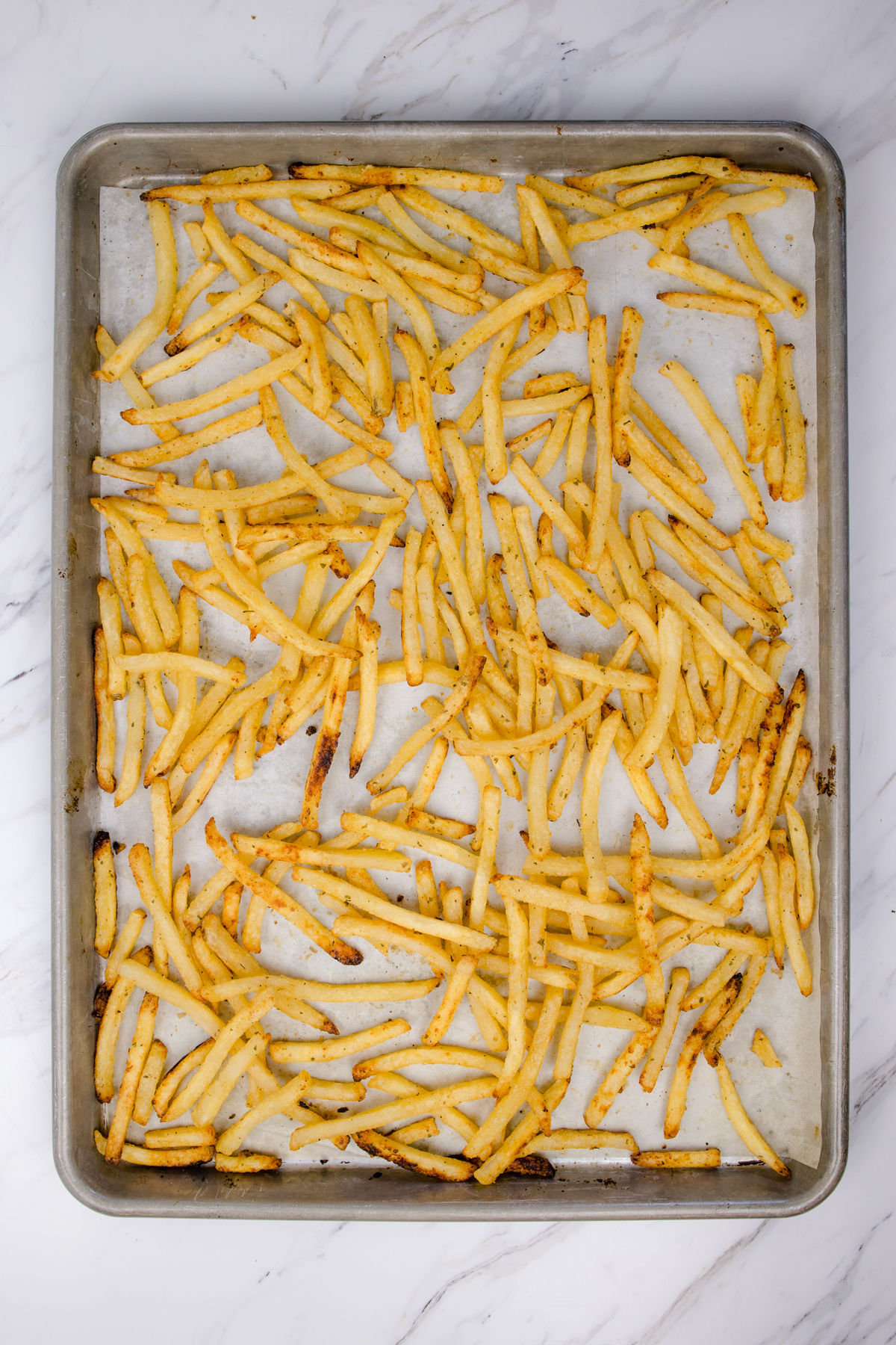 Top view of a baking tray filled with seasoned and part-baked fries. 