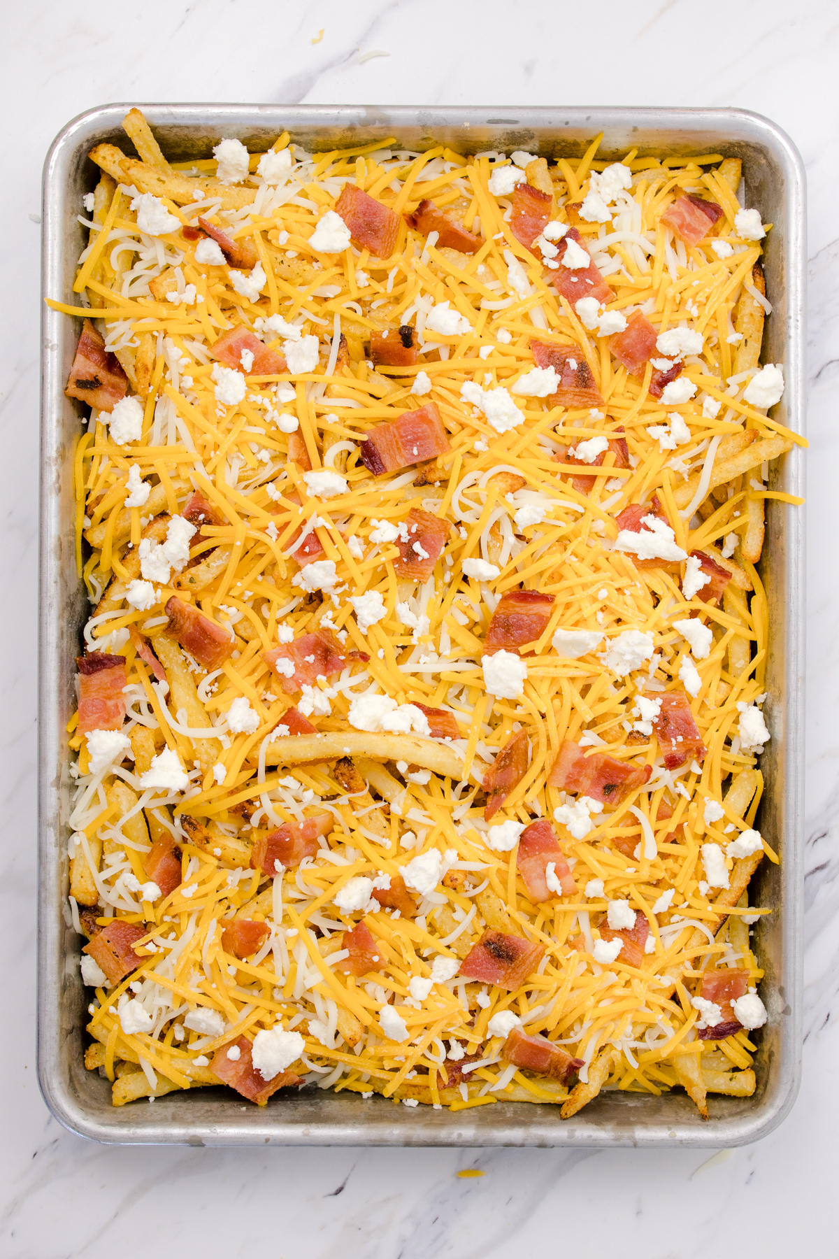 Top view of Bacon Cheese Fries on a baking tray before being baked. 