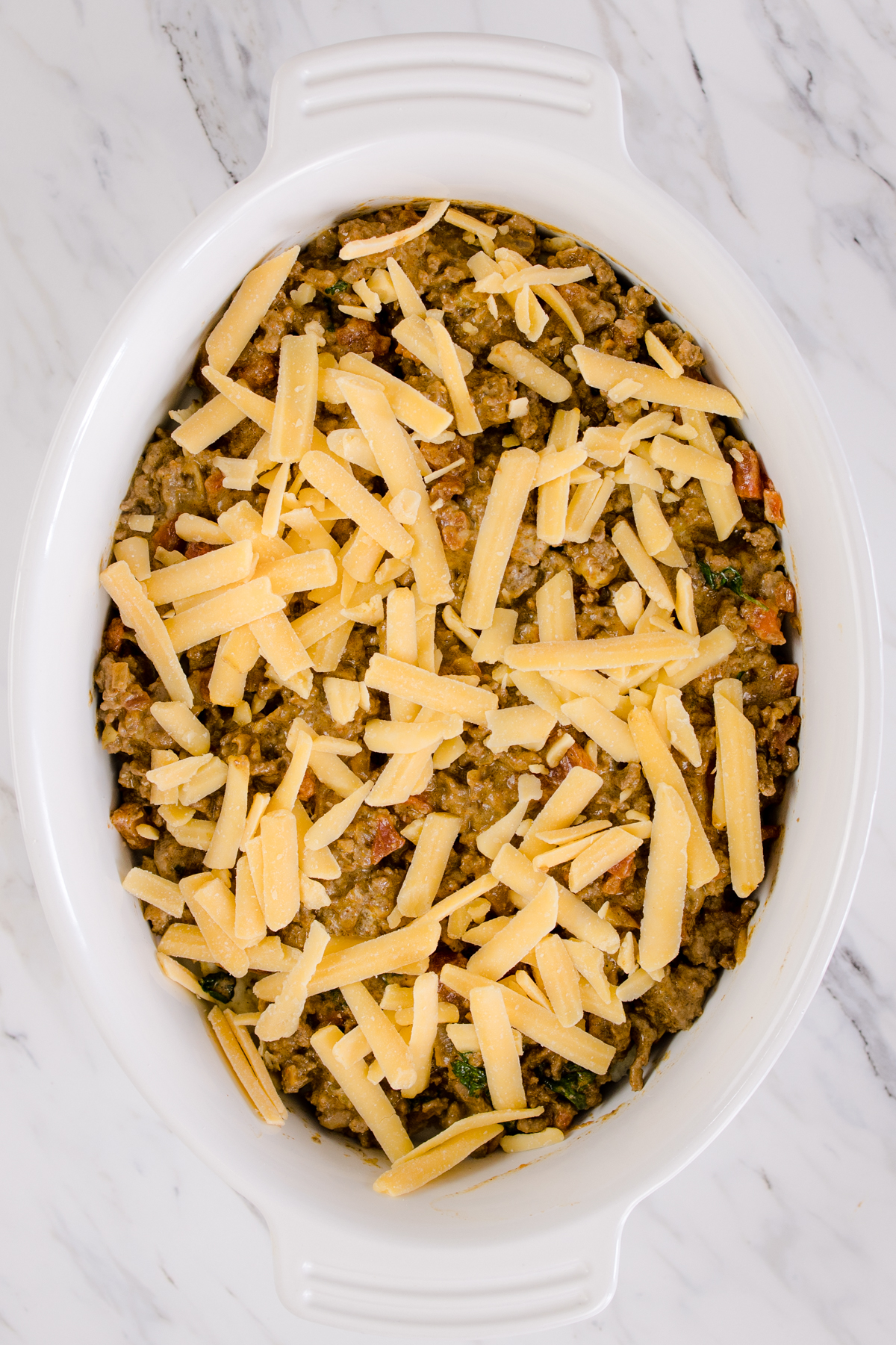 Top view of casserole dish with a layer of pasta on top of a ground beef layer. 
