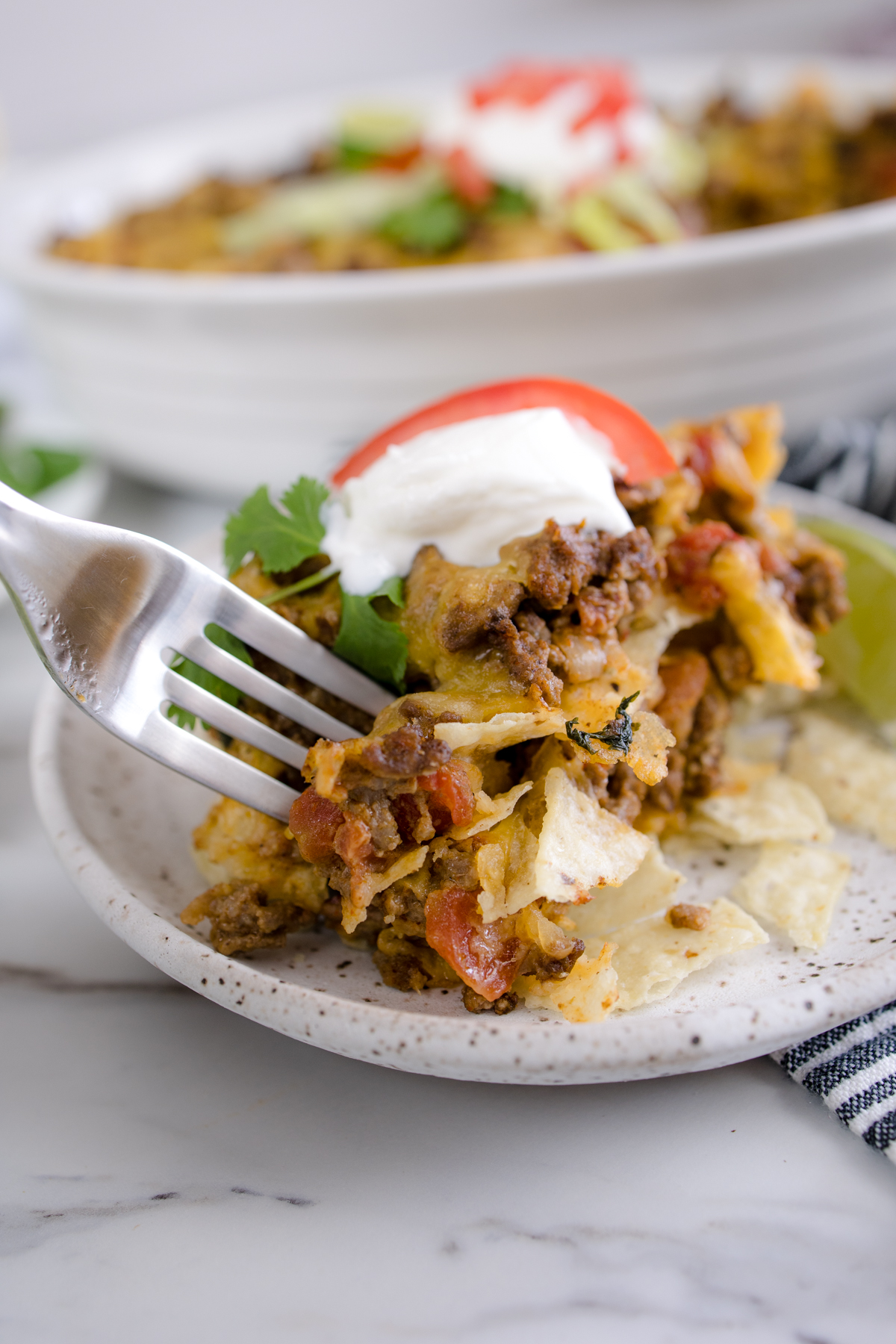 Close-up of a spoonful of Taco Casserole on a white plate with a fork stuck into it. 