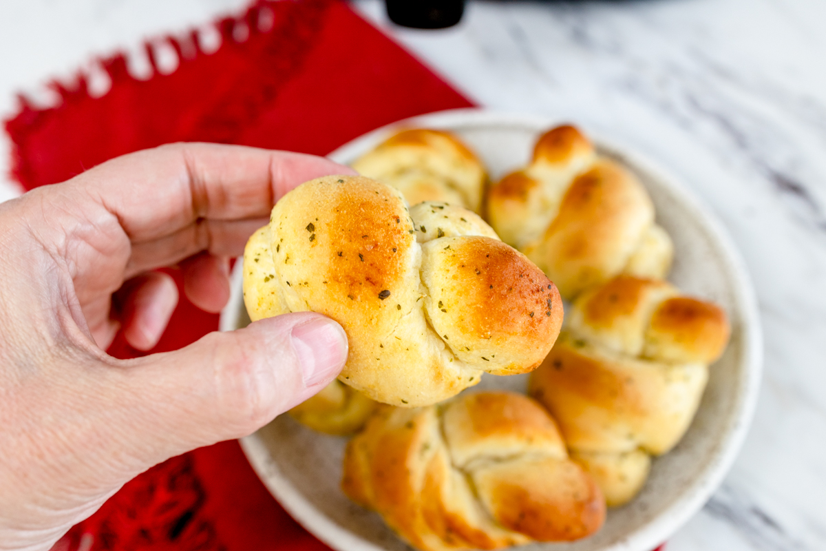 Close up top view of a plate filled with garlic knots with a hand reaching in and picking one up. 