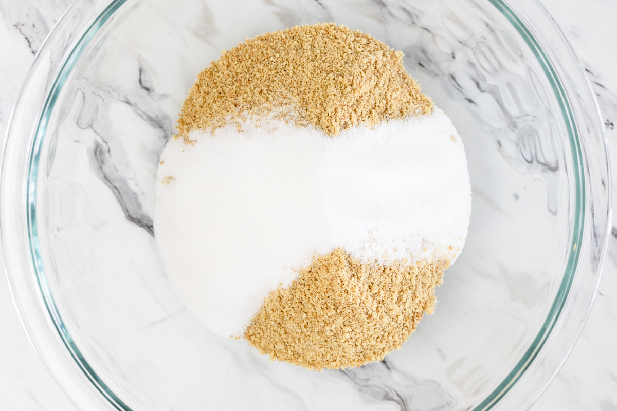 Top view of glass mixing bowl with graham cracker crumbs in it and sugar on top. 