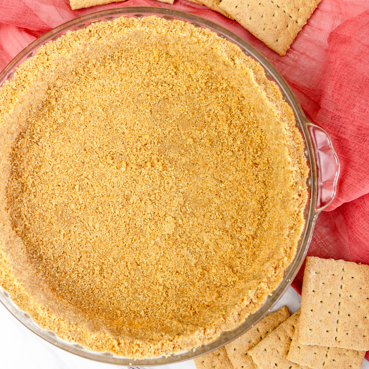 Top view of Homemade Graham Cracker Crust in a glass piw dish on top of a table with a red tea towel.