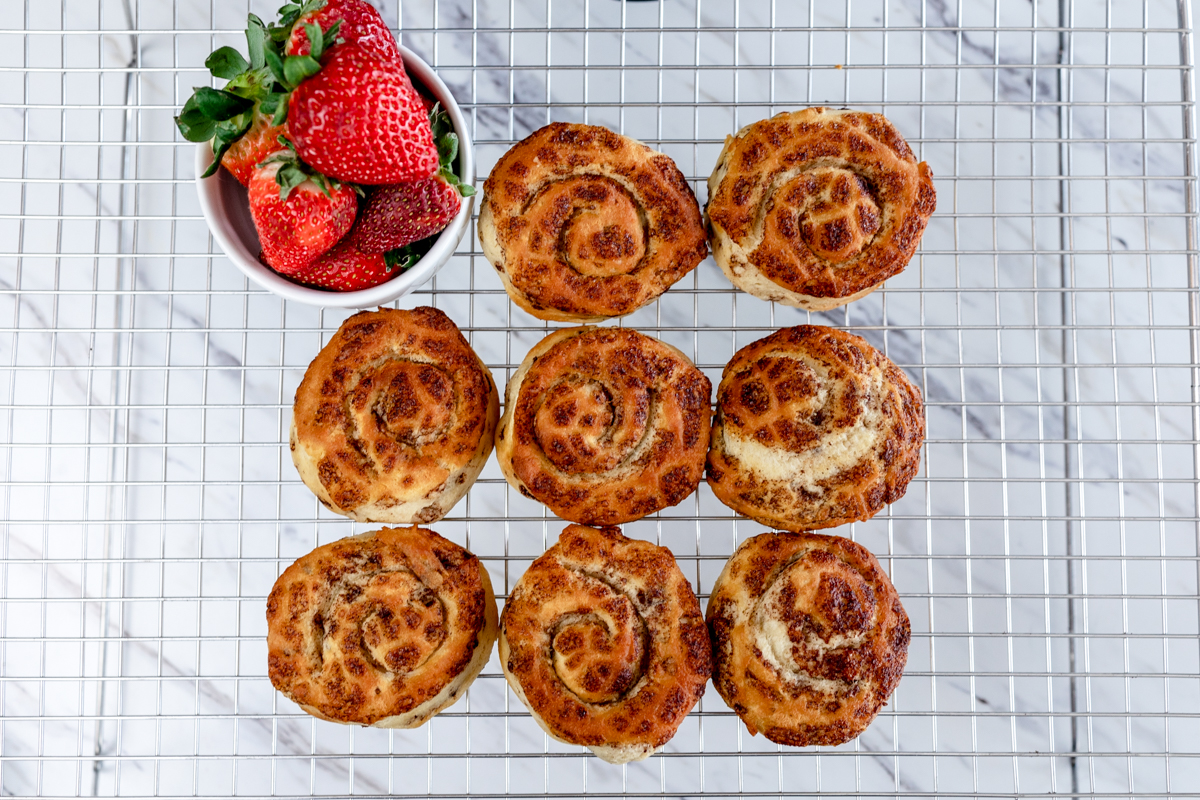 Top view of freshly baked cinnamon rolls on a wire rack with a small bowl of fresh strawberries next to it. 