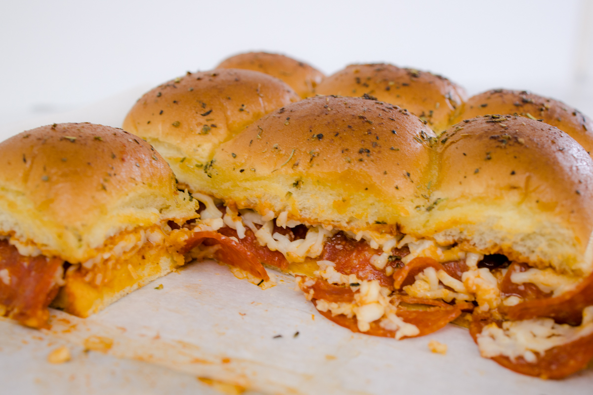 Close up of baked pizza sliders on a baking sheet, with some of them missing. 