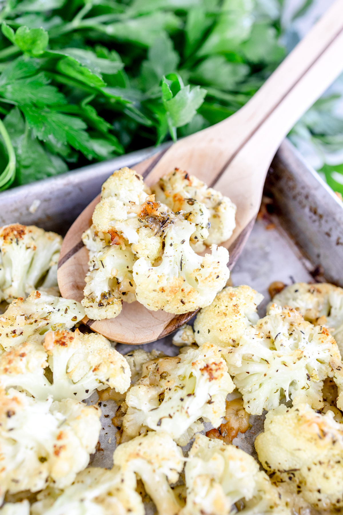 Roasted cauliflower in a baking pan being lifted out with a wooden spoon. 