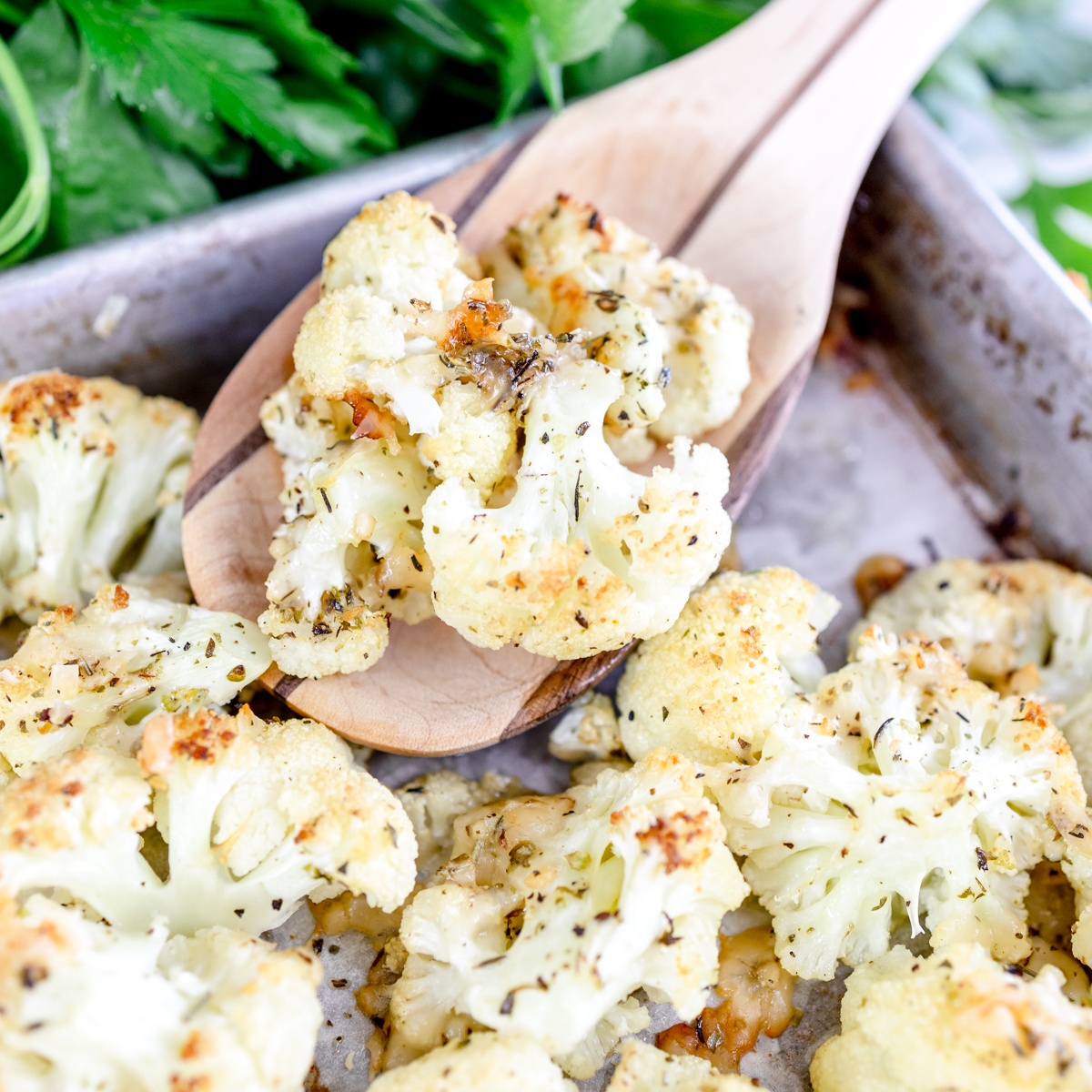 Close-up of Roasted Cauliflower with Parmesan cheese on a baking tray with a wooden spoon in it.
