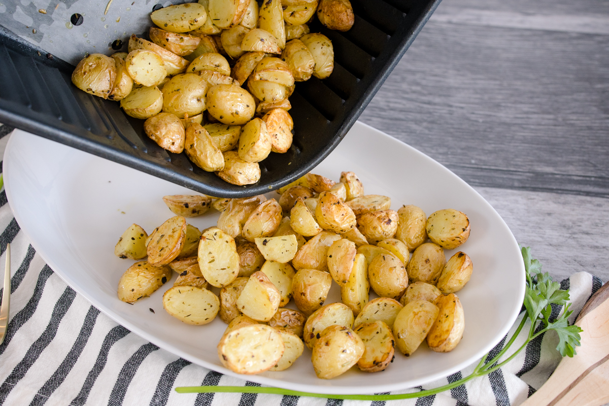 Roasted potatoes being poured onto a serving bowl from an air fryer basket.
