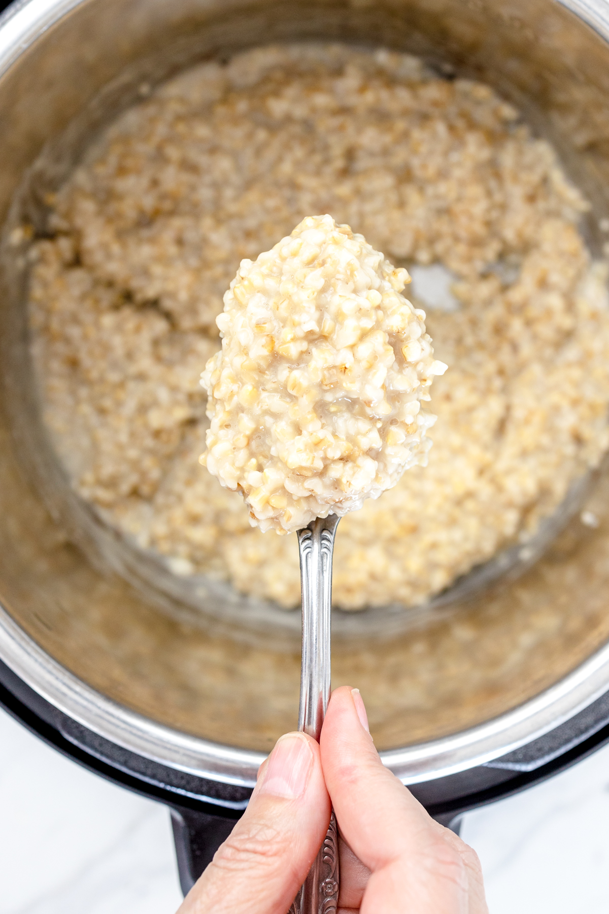 Top view of an Instant Pot with steel cut oats in it and a spoonful of oats being lifted out of it. 
