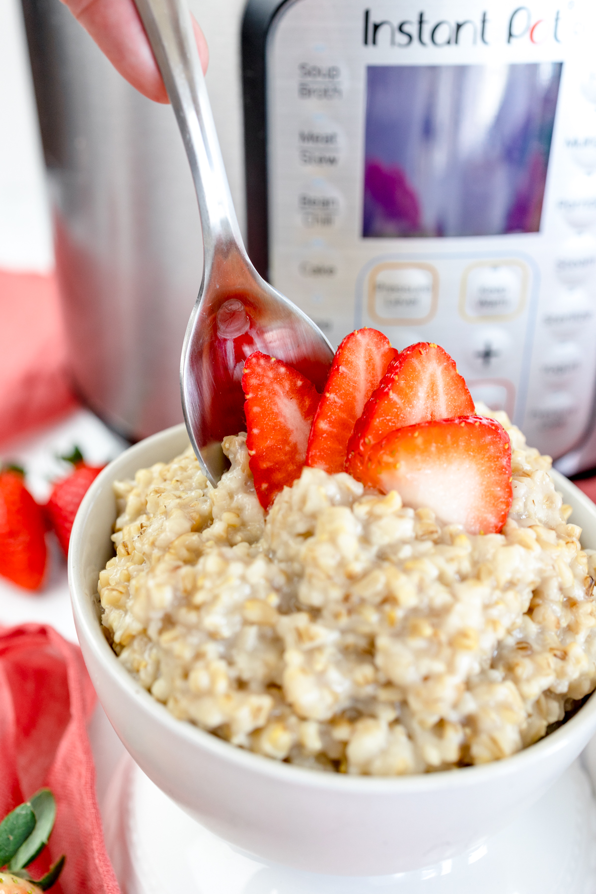 Close up of a bowl of steel cut oats with a spoon in it and sliced strawberries on top in front of an Instant Pot.  