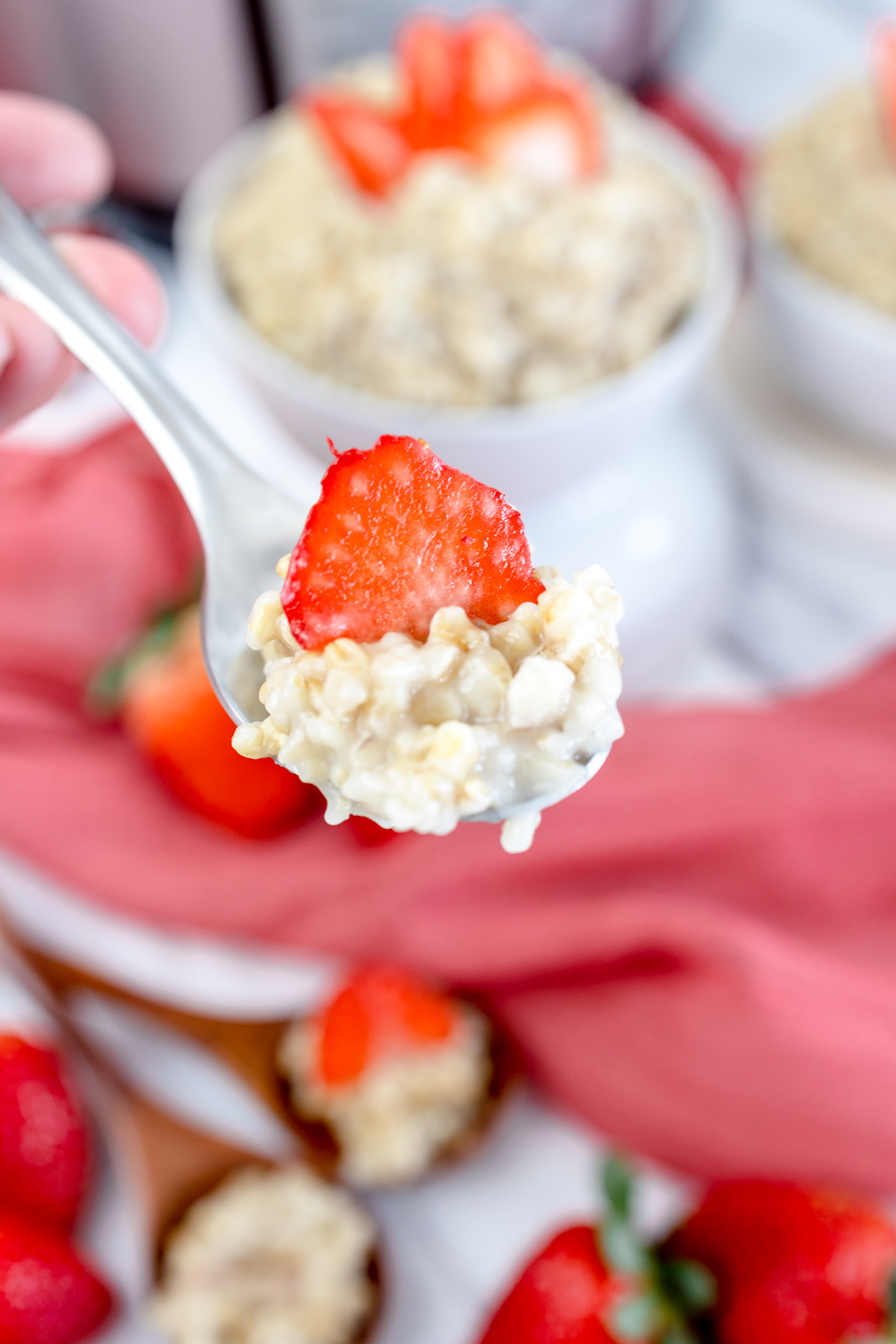 Close up of a spoon full of steel cut oat porridge with a slice of strawberry on top. 