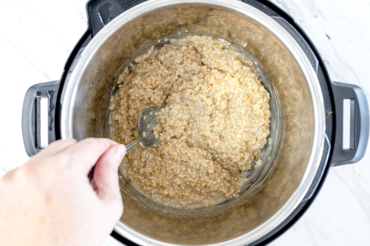 Top view of Instant Pot with oats and water in it, being stirred by a metal spoon. 