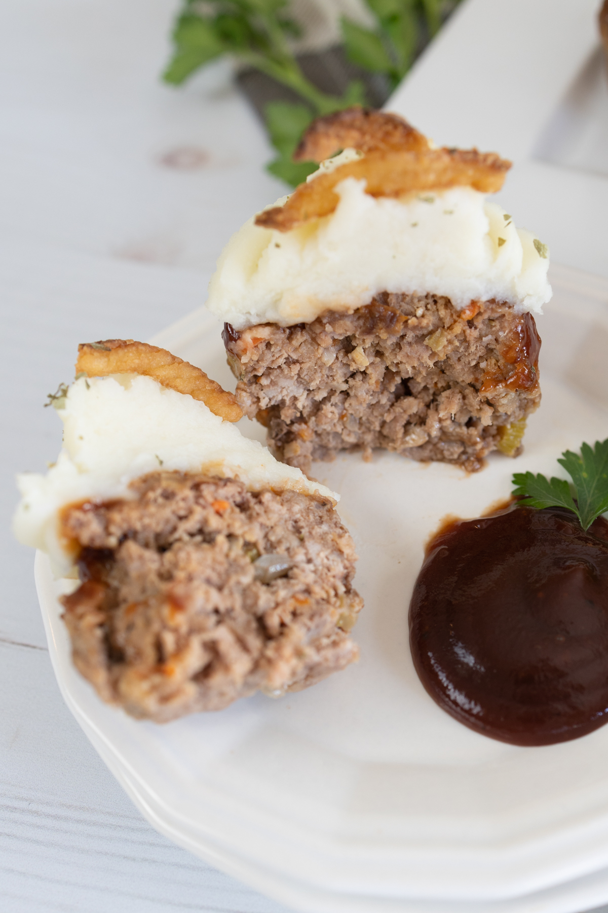 Top view of two meatloaf muffin halves lying on a plate with brown sauce next to them, 