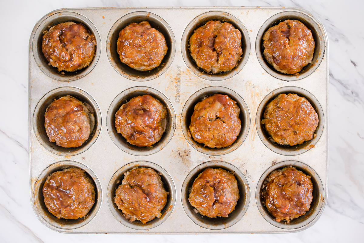 Top view of a muffin tin with balls of meatloaf in each cup. 
