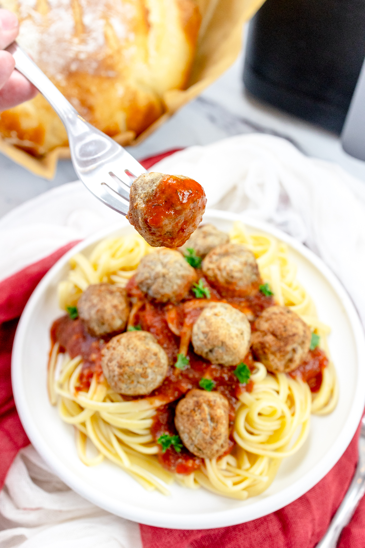 A plate of spaghetti meatballs with one meatball on a fork held over the plate.