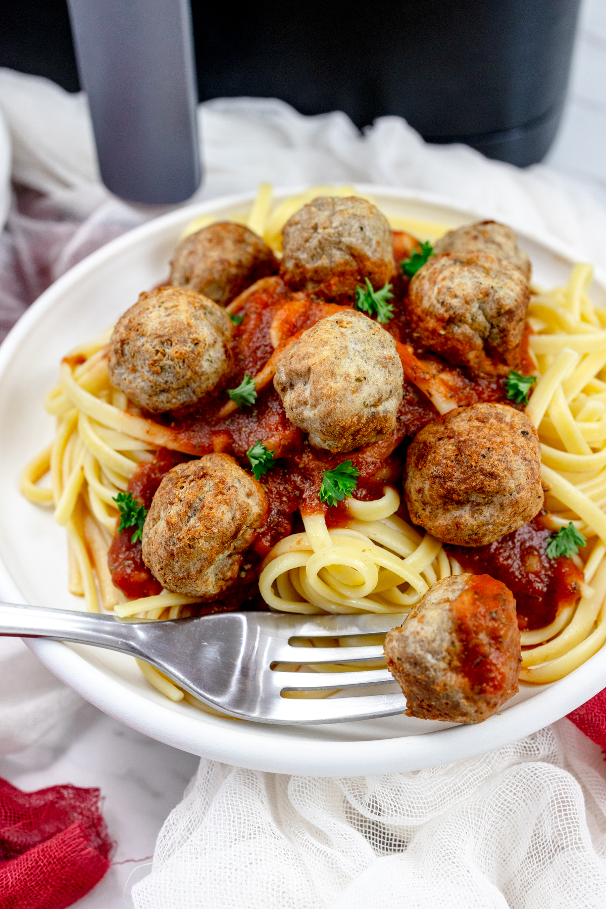 A plate of spaghetti meatballs in front of an air fryer.