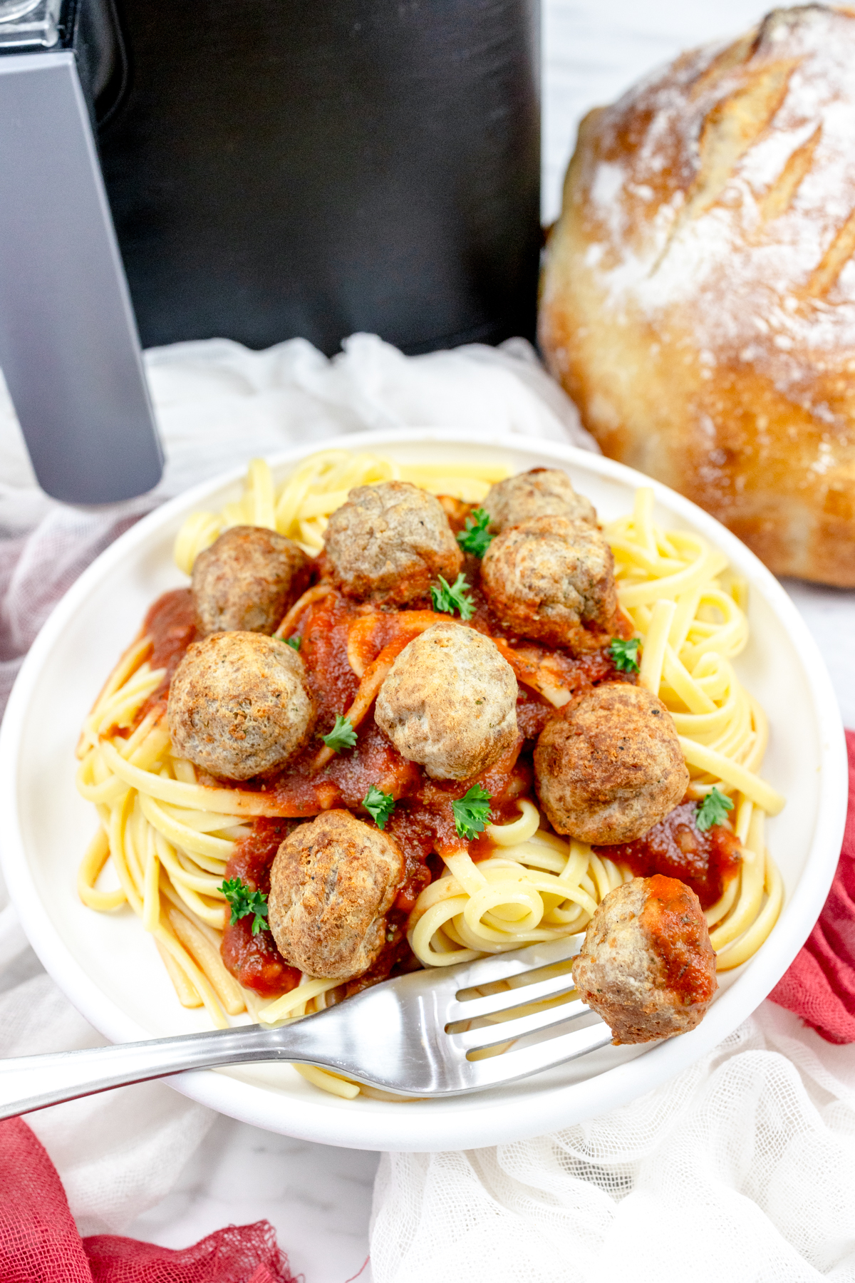 A plate of spaghetti meatballs in front of an air fryer.