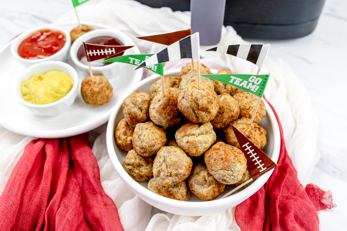 A bowl of meatballs in front of an air fryer with a plate next to it that has 3 ramekins of different sauces.