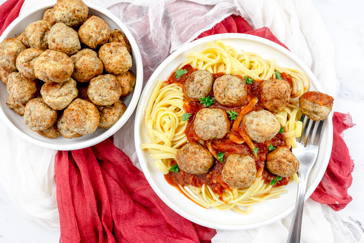 Close up view of a plate of spaghetti meatballs next to a bowl of meatballs.