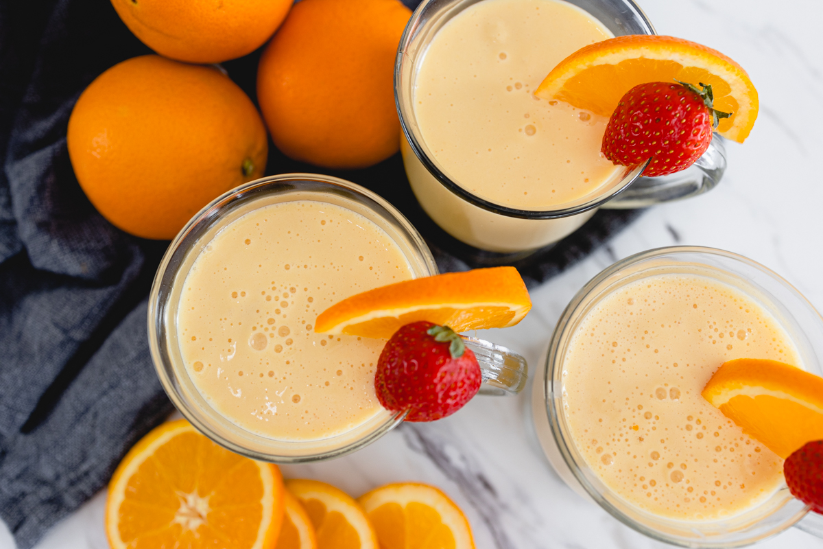 Top view of three glass mugs of Orange Julius with a strawberry and a slice of orange on the side.
