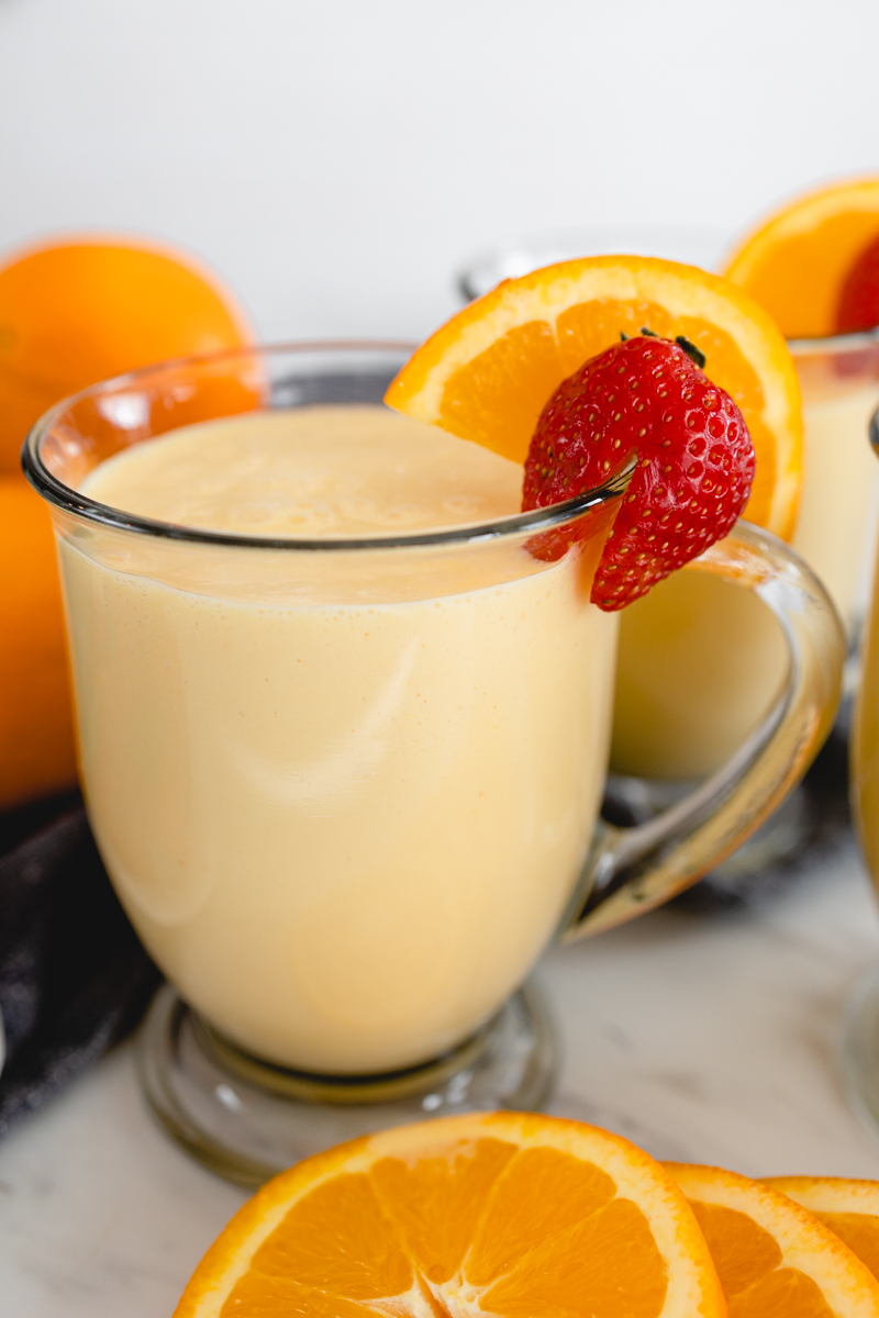 A glass mug of Orange Julius with a strawberry and a slice of orange on the side.