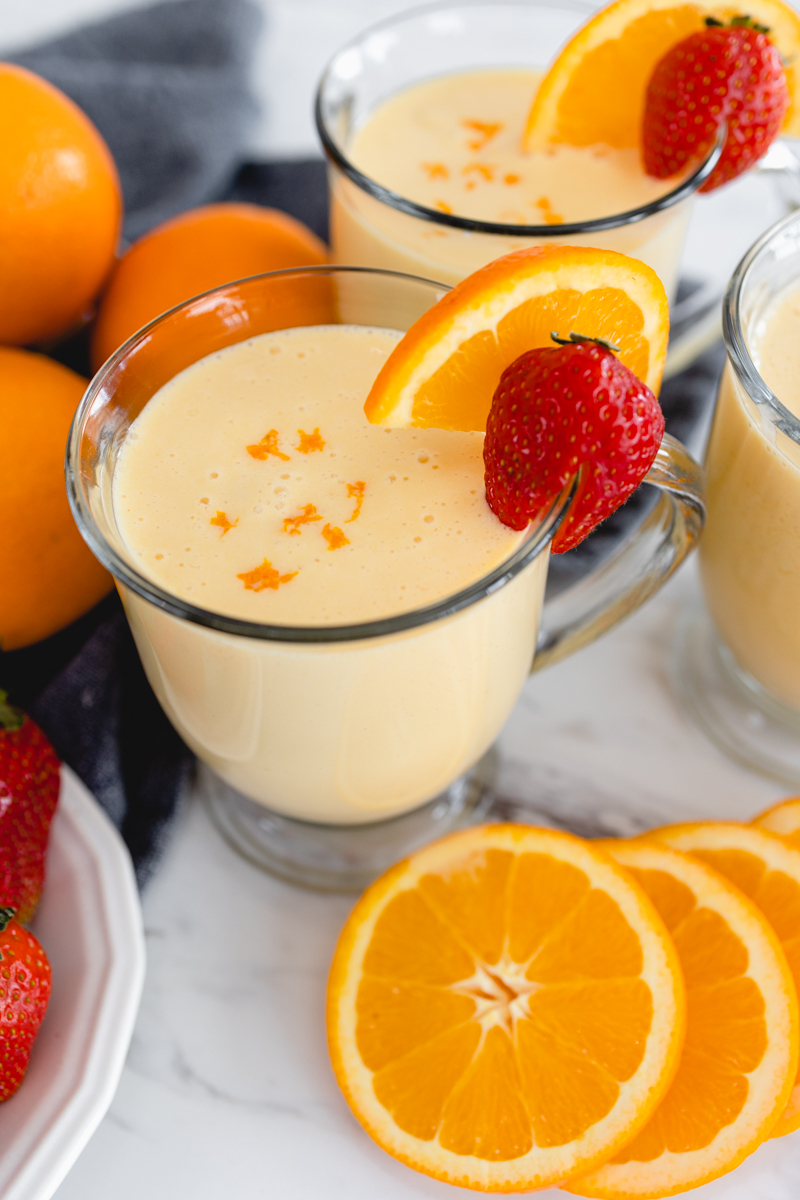 A glass mug of Orange Julius with a strawberry and a slice of orange on the side.