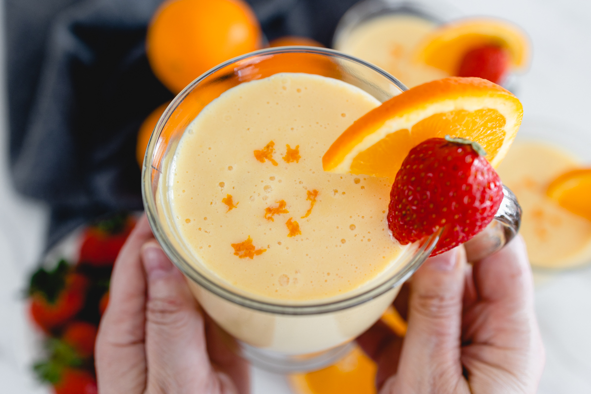 A glass mug of Orange Julius with a strawberry and a slice of orange on the side.