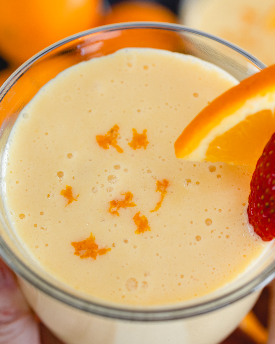Close up of a glass mug of Orange Julius with a strawberry and a slice of orange on the side.