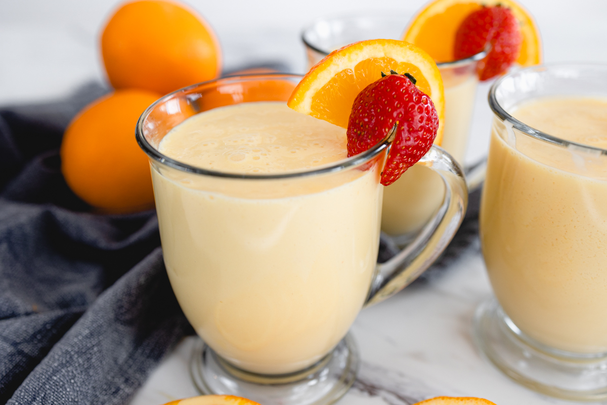 A glass mug of Orange Julius with a strawberry and a slice of orange on the side.