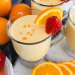 A glass mug of Orange Julius with a strawberry and a slice of orange on the side.