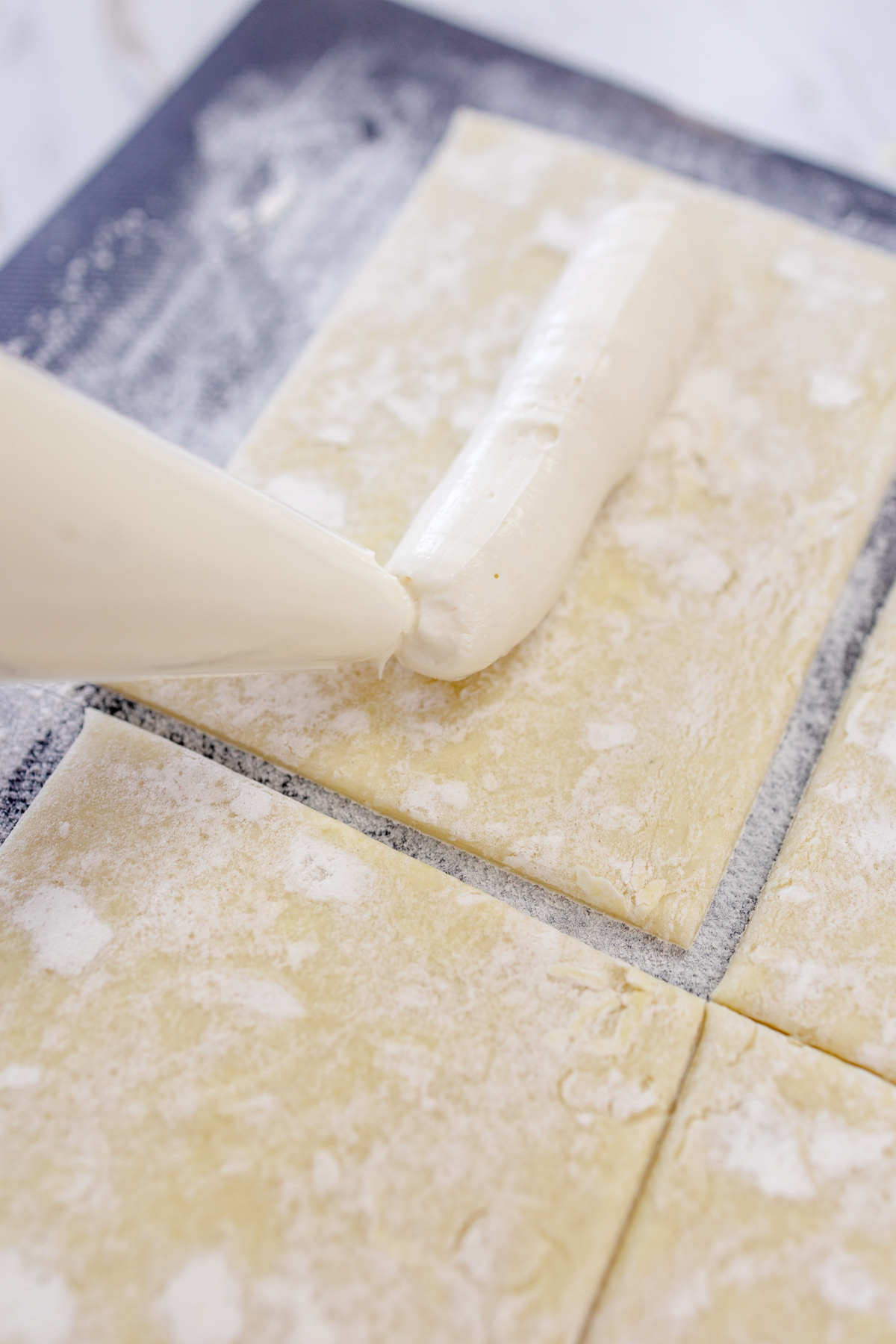 Close up of cream cheese mixture being piped onto rectangle pieces of pastry.