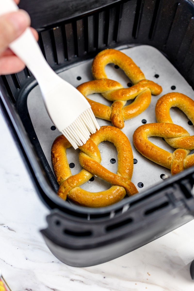 Pretzels in the air fryer being brushed with oil before frying.