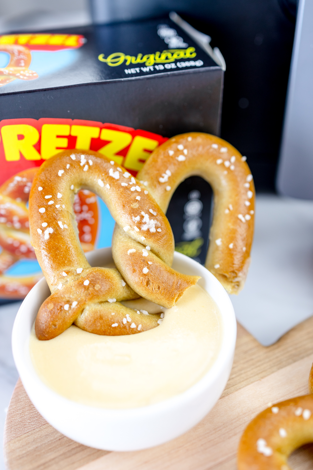 Air-fried pretzel dipped in sauce, with a box of Super Pretzel brand frozen pretzels in the background.