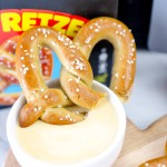 Air-fried pretzel dipped in sauce, with a box of Super Pretzel brand frozen pretzels in the background.