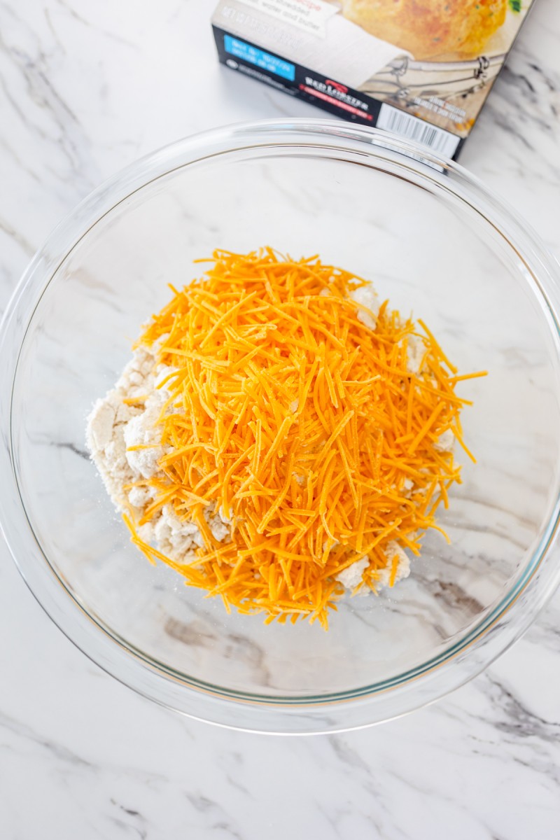 Top view of a glass mixing bowl with biscuit mix and cheddar cheese on top.