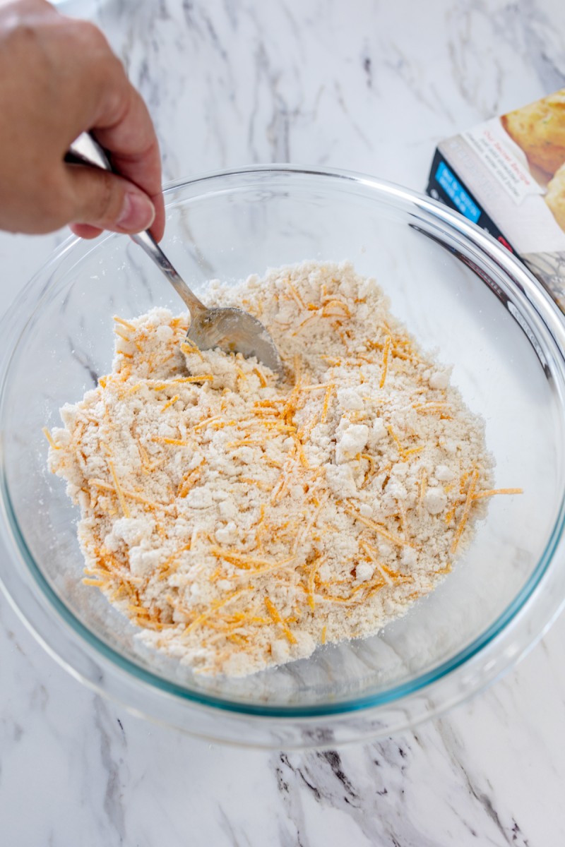 Close up of a glass mixing bowl with cheddar bay biscuit mix in it being mixed with a fork.