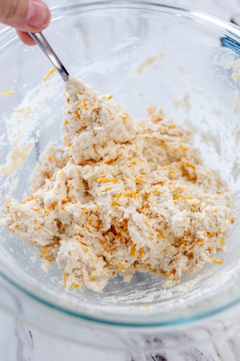Close up of a glass mixing bowl with cheddar bay biscuit dough in it being mixed with a fork.
