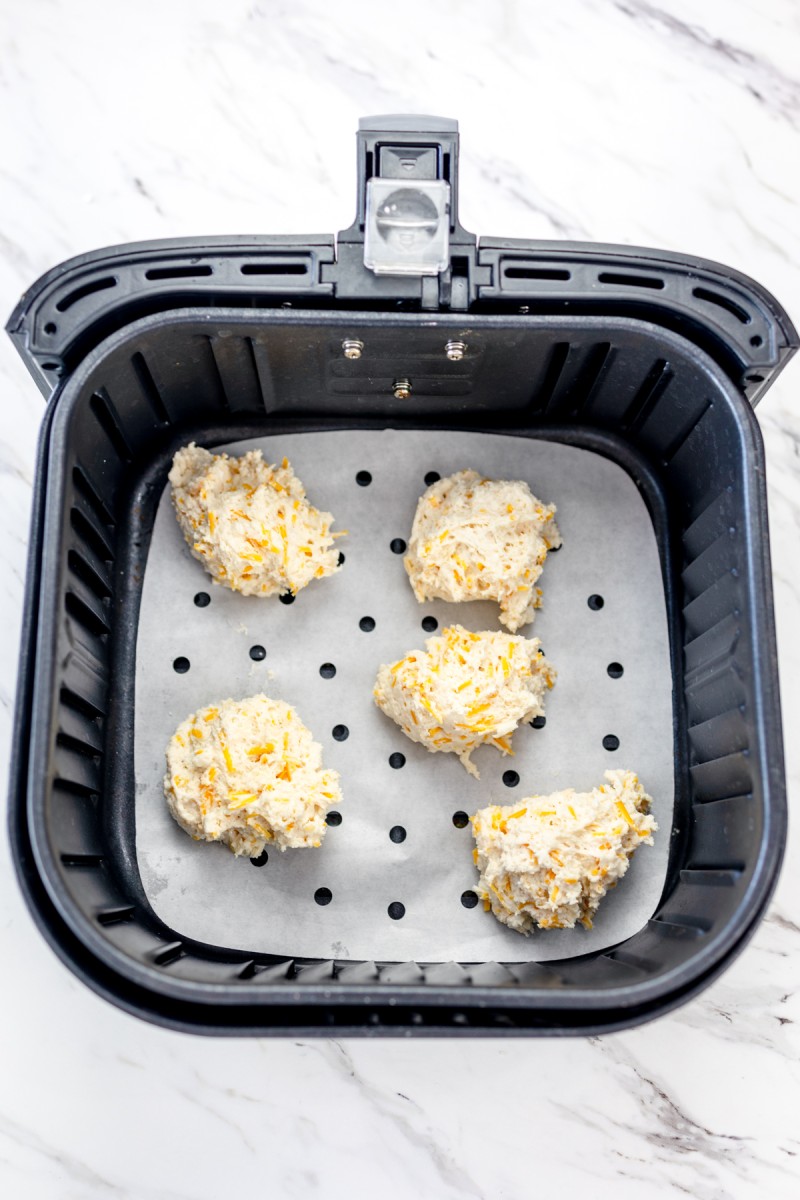 Top view of raw cheddar bay biscuits in the tray of an Air Fryer on parchment paper.
