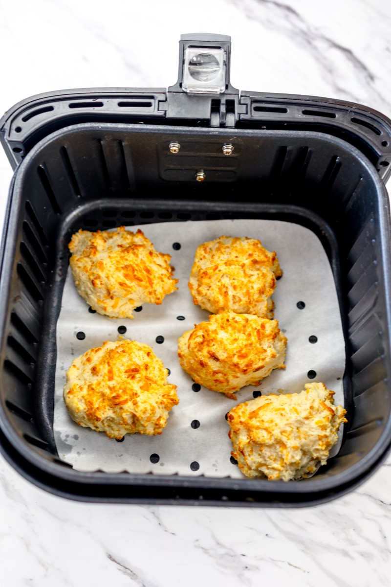 Top view of cooked cheddar bay biscuits in the tray of an Air Fryer on parchment paper.
