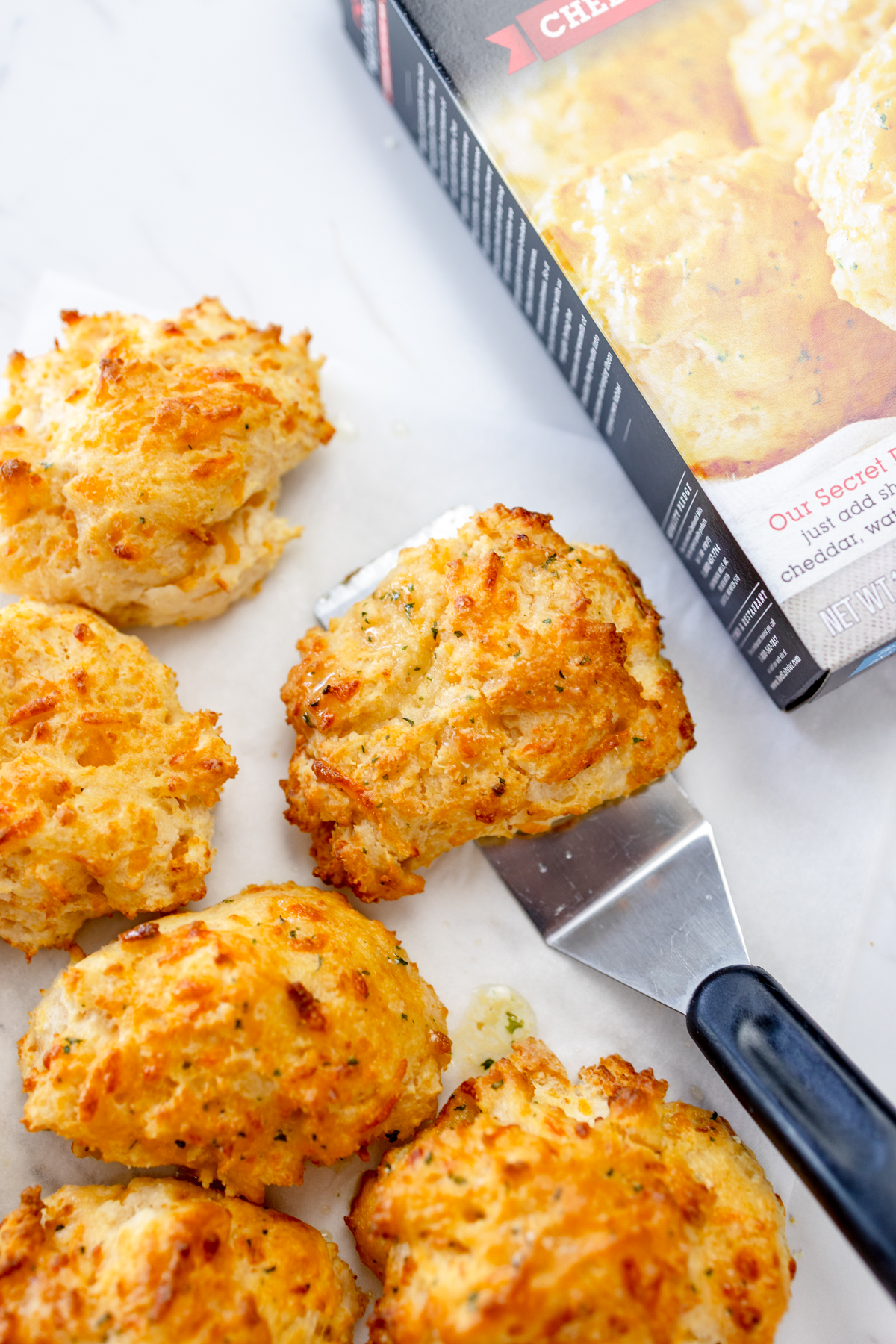 Top view of Red Lobster Cheddar Bay Biscuits on a white surface, one being scooped up with a spatula.